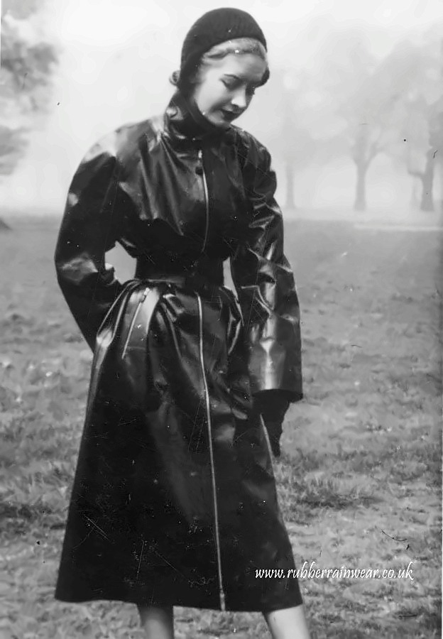 Woman in a long belted black mackintosh and knitted hat walking through a misty park.